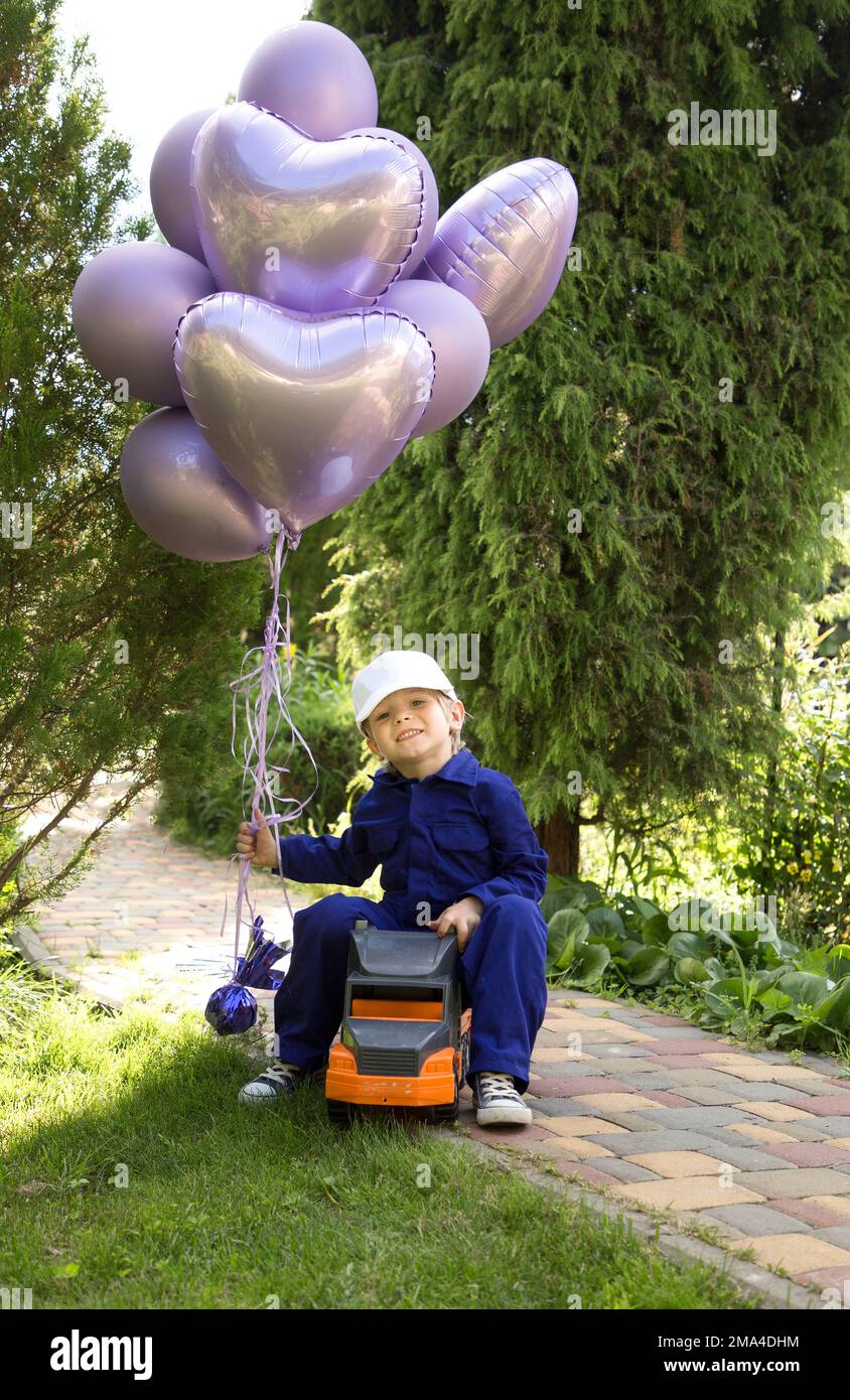boy of 5-6 years old is sitting cheerfully on a large toy car, holding