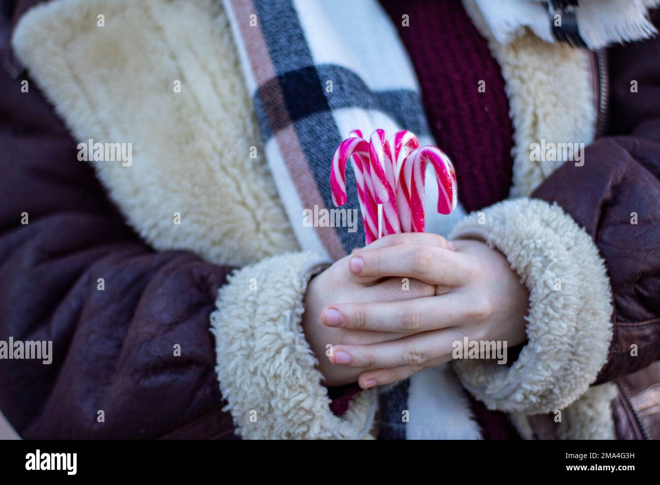 Woman clutching candy canes as she walks around Madrid warm in a coat and scarf in winter. Stock Photo
