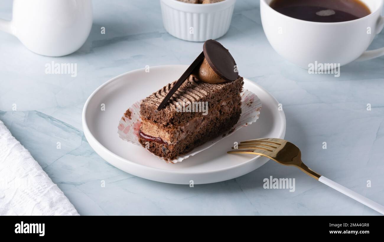 Delicious chocolate cake on plate and coffee on light table Stock Photo