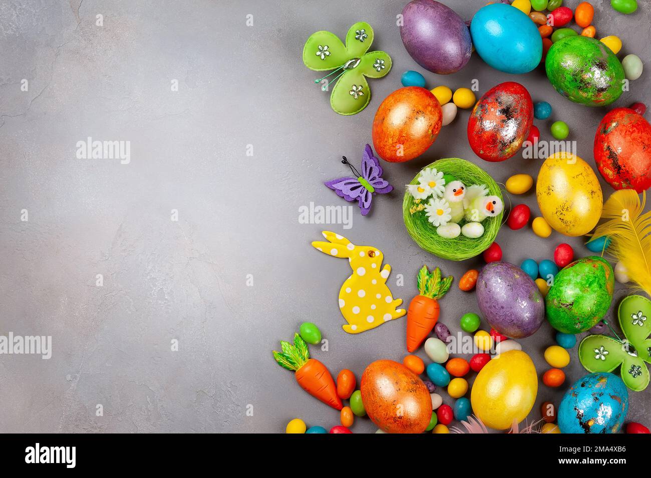 Colorful Easter eggs,chocolate Easter sweets, bunny and nest with chicks  on grey background. Top view with copy space. Festive Easter concept. Stock Photo