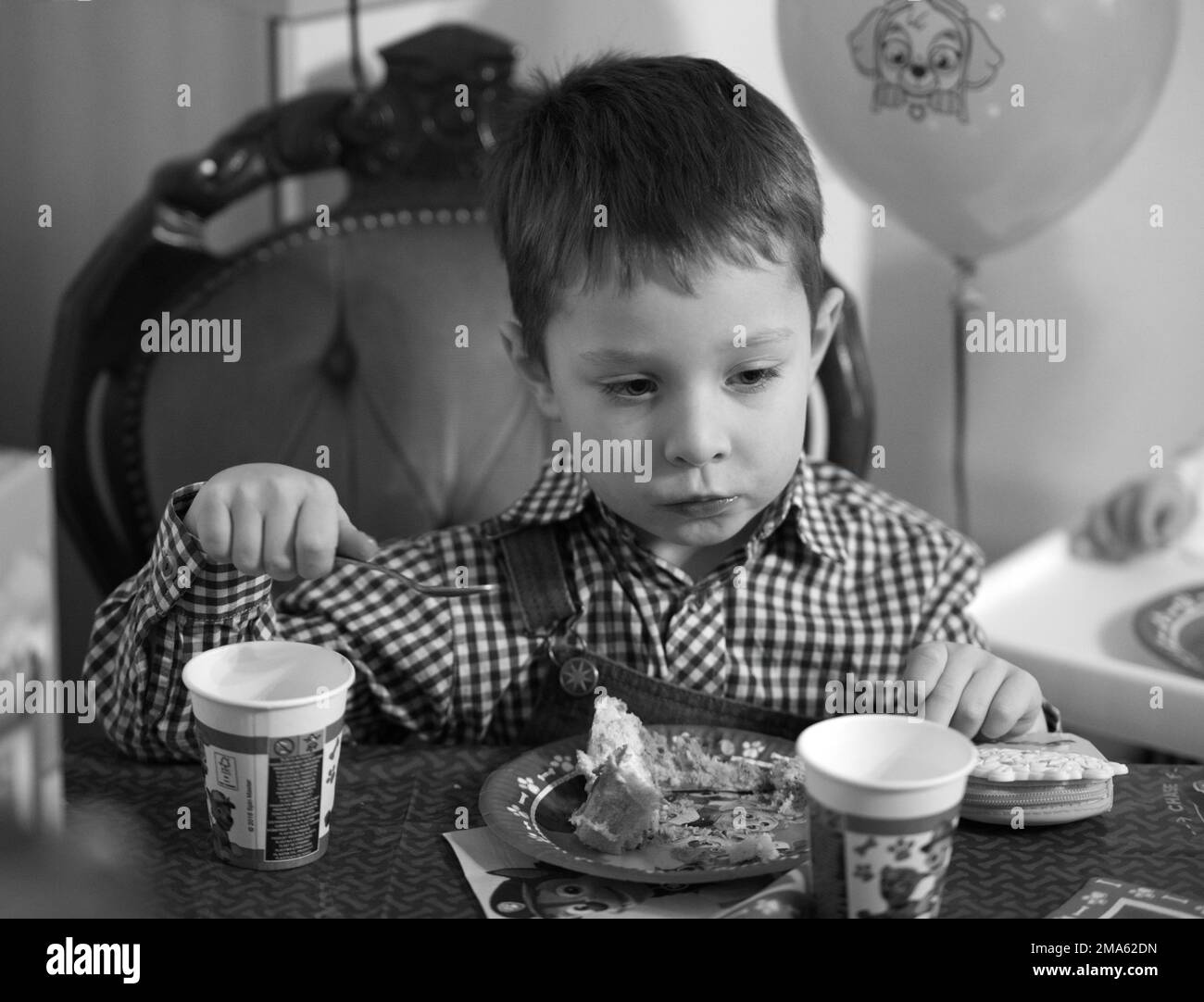 A grayscale of a little boy eating cake sitting around the table Stock Photo Alamy