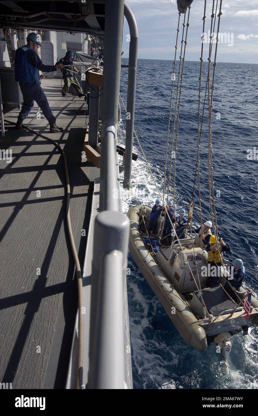 050622-N-5781F-024. [Complete] Scene Caption: US Navy (USN) deck department Sailors, Ticonderoga Class Guided Missile Cruiser USS COWPENS (CG 63), tend lines while retrieving a USN Rigid Hull Inflatable Boat (RHIB) from the Coral Sea after conducting small boat exercises. The COWPENS is accompanying the USN Aircraft Carrier USS KITTY HAWK (CV 63) and other ships of the Kitty Hawk Carrier Strike Group (CSG), as part of Exercise TALISMAN SABER 2005. TALISMAN SABRE is an exercise jointly sponsored by the US Pacific Command (USPACOM) and Australian Defense Force Joint Operations Command, and desig Stock Photo