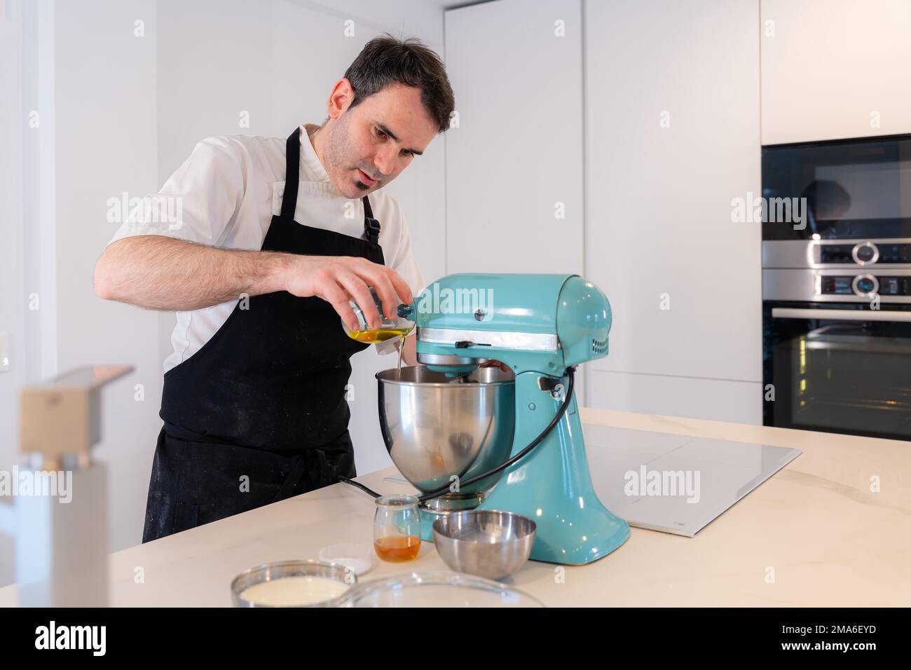 A man baker bakes a red velvet cake at home, preparing the cake by adding oil in the food processor, work at home Stock Photo