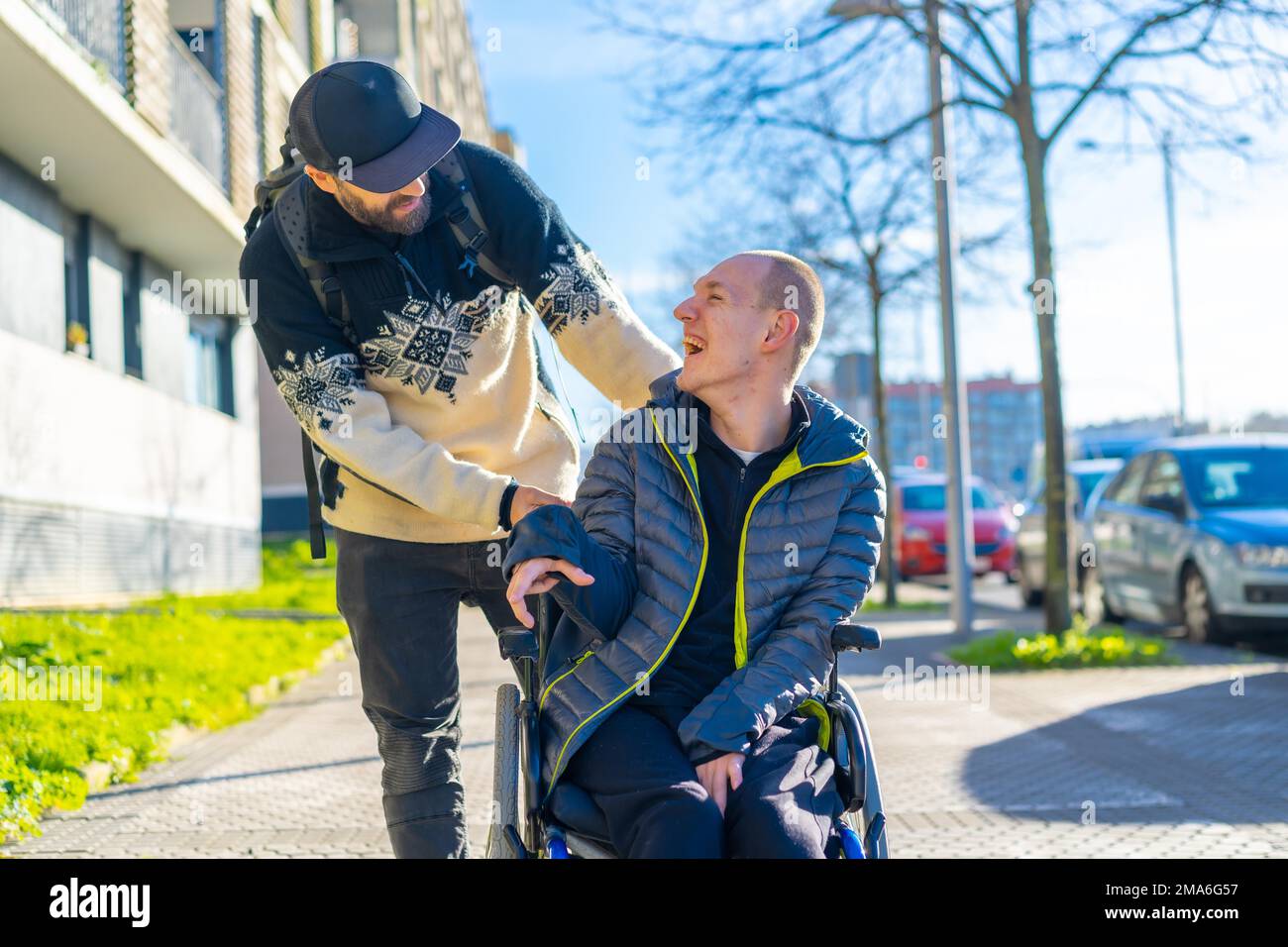 A disabled person in a wheelchair with a friend smiling, handicapped normality Stock Photo