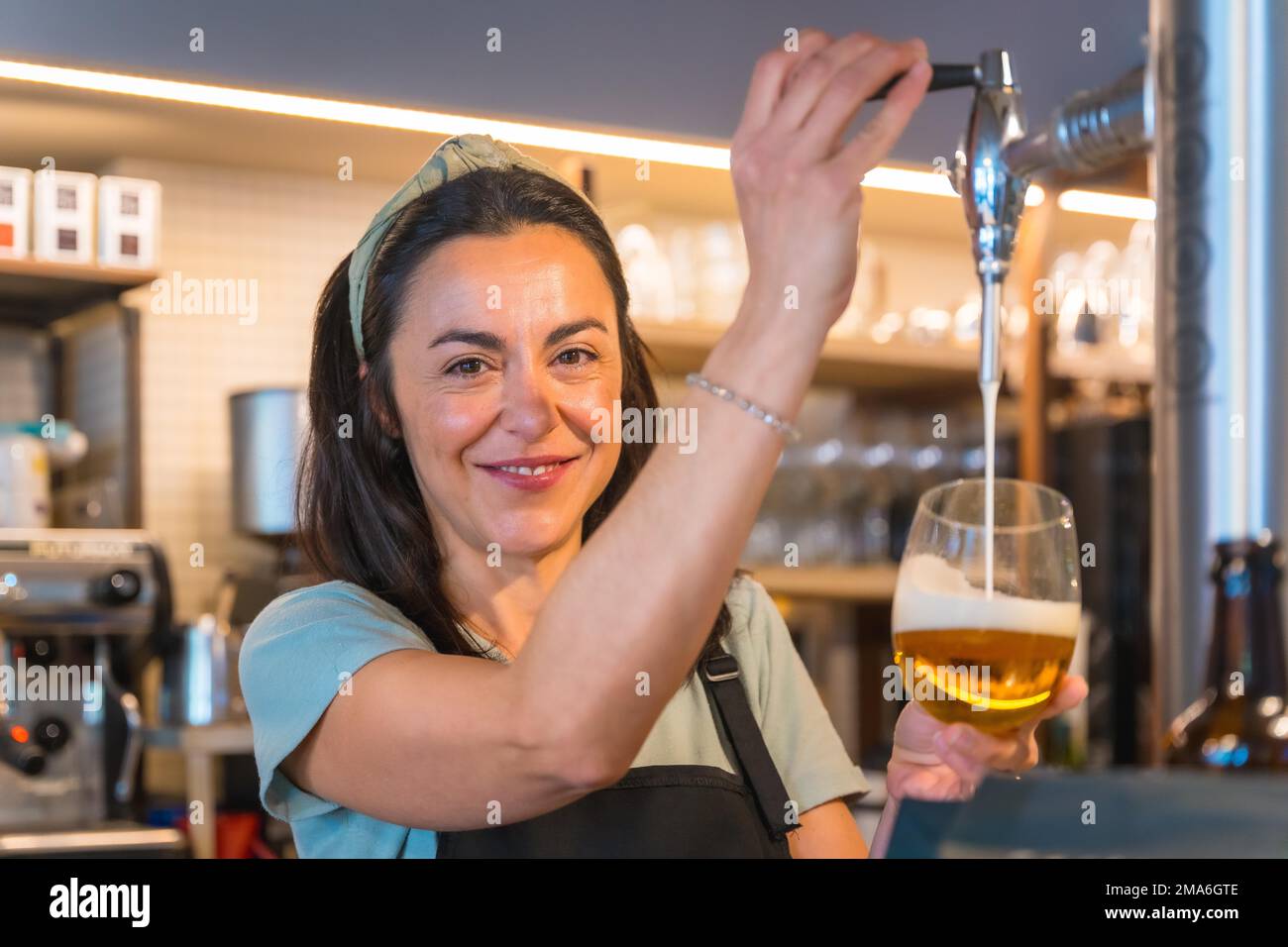 Smiling waitress brewing a blonde beer in a tap, covid restrictions are lifted and the mandatory use of face masks is removed Stock Photo