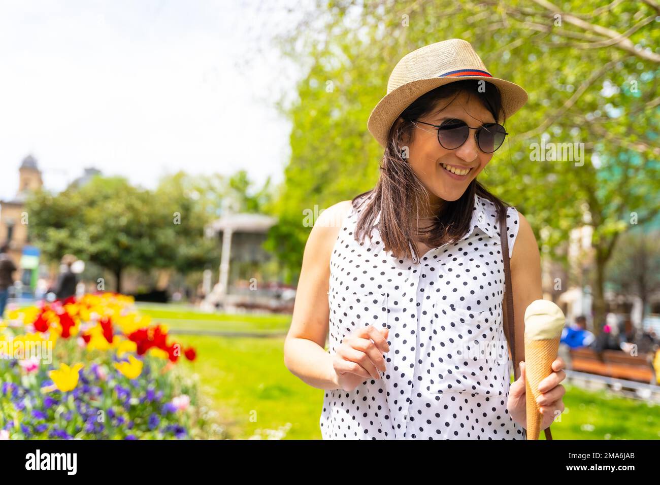 A tourist woman visiting the city eating an ice cream cone, smiling enjoying vacations, solo female traveler concept, wearing sunglasses and a hat Stock Photo