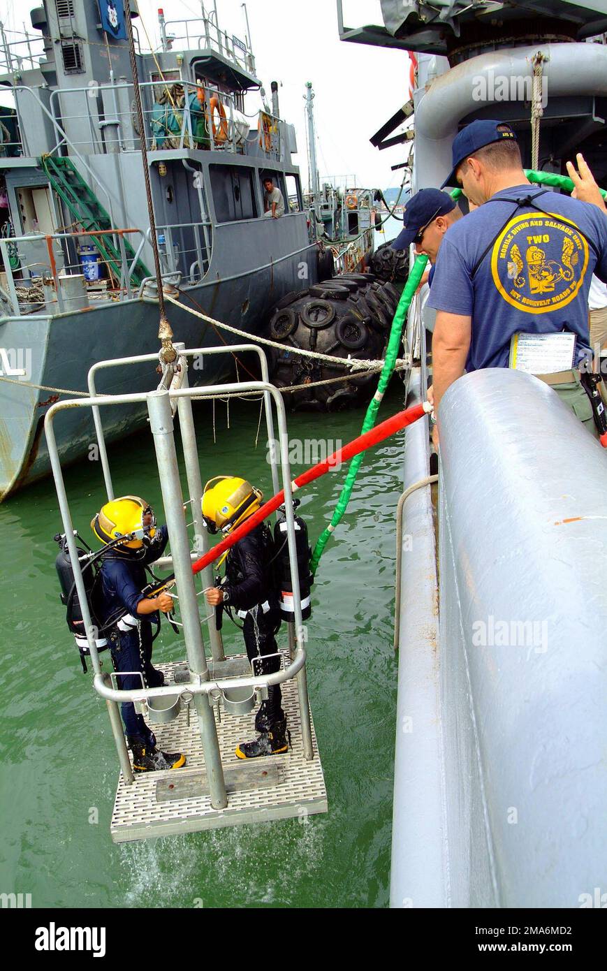 Two Royal Brunei Navy (RBN) Divers stand aboard a diving cage while being lowered into the water from the US Navy (USN) Salvage Ship, USS SAFEGUARD (ARS 50) during familiarization dives conducted during the Brunei phase of Cooperation Afloat Readiness and Training (CARAT). CARAT is an annual series of bilateral military training exercises with several Southeast Asian nations designed to enhance interoperability of the respective sea services. Base: USS Safeguard (ARS 50) Country: Brunei Darussalam (BRN) Stock Photo