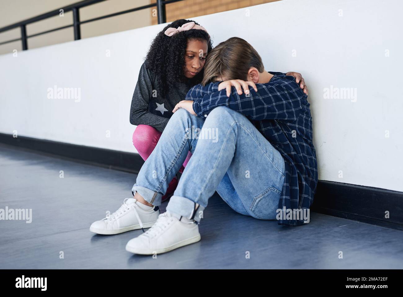 Are you okay. Full length shot of an unrecognizable boy sitting in the school hallway and feeling depressed while a classmate comforts him. Stock Photo