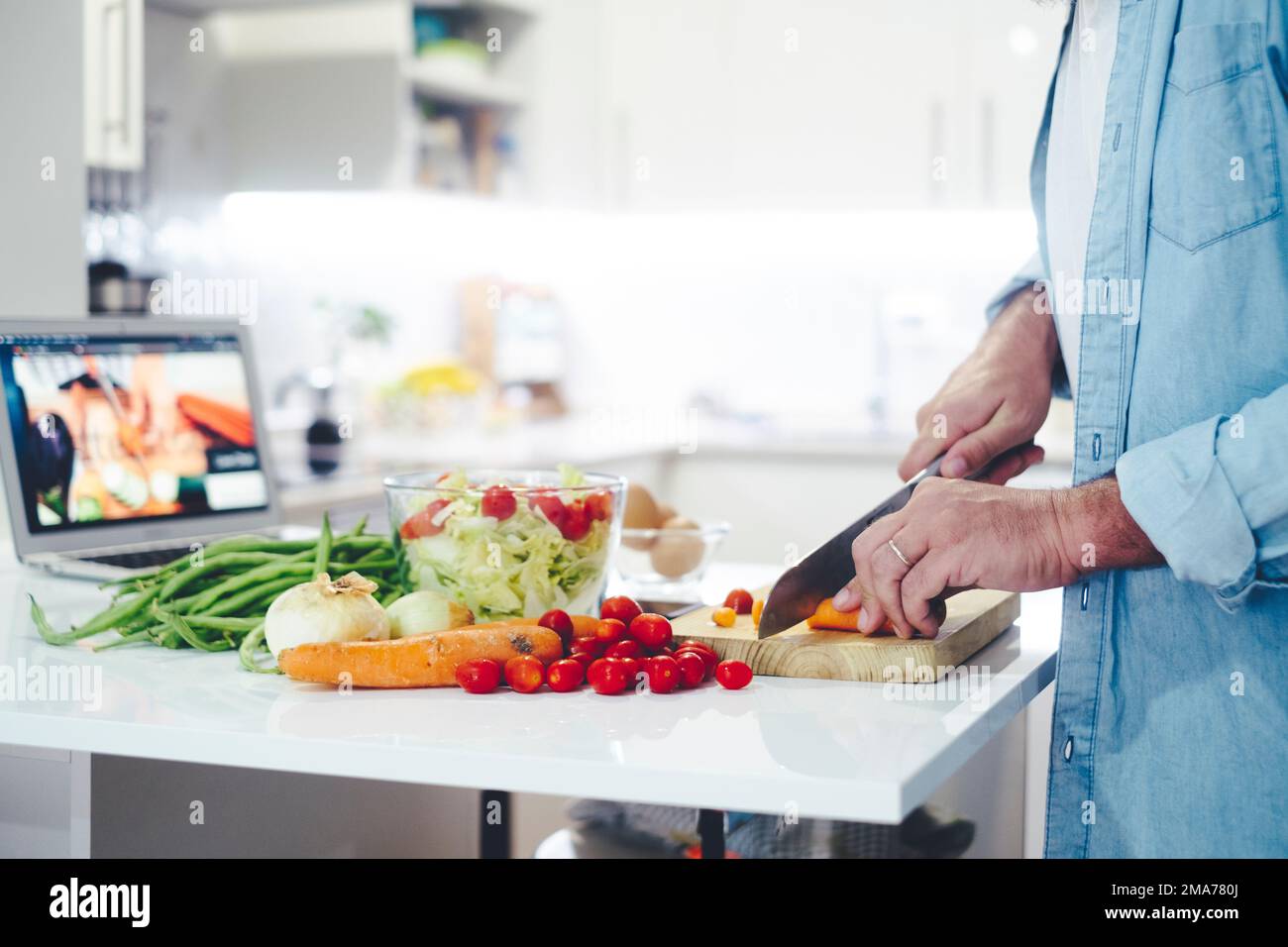 One man watching video recipe on laptop while cooking vegetables in