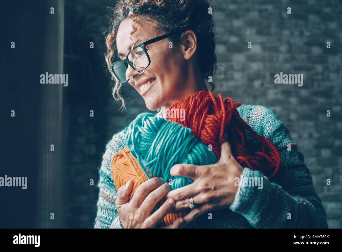 One woman with pleasure expression on face holding with love a bunch of wool balls in different color. Concept of indoor leisure activity and hobby. F Stock Photo
