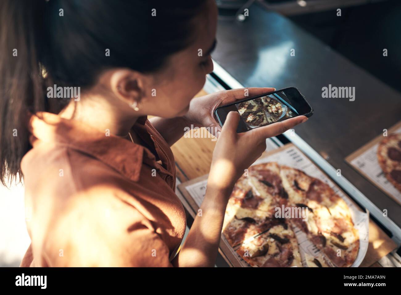 Todays lunch deserves a shoutout. an unrecognizable woman standing alone and using her cellphone to photograph her pizza at a restaurant. Stock Photo