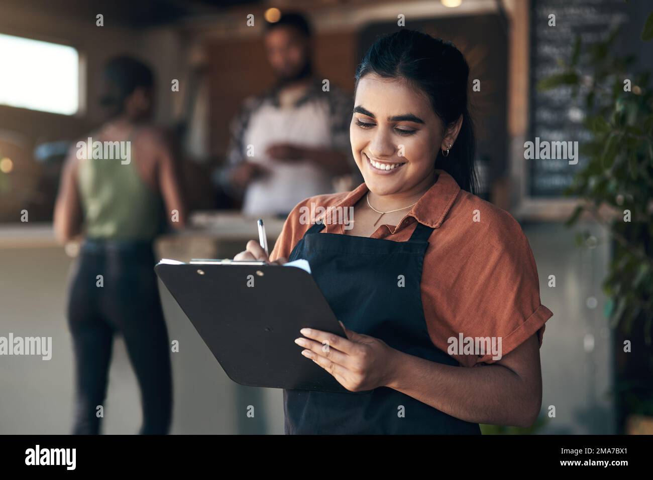 Ill reserve that table for you. an attractive young woman standing outside her restaurant and holding a clipboard. Stock Photo
