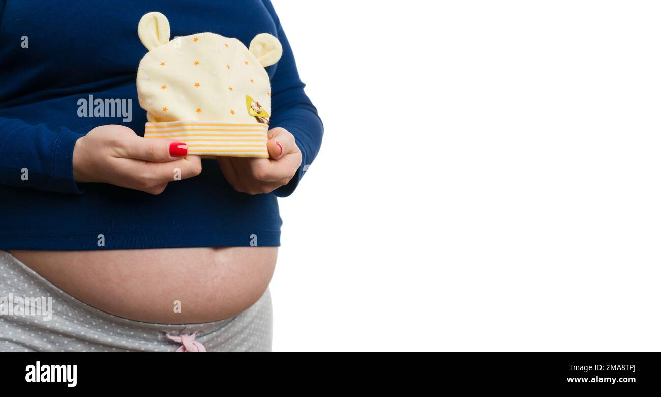 Close-up of pregnant woman holding baby yellow hat with stars and bear ears isolated on white studio background Stock Photo