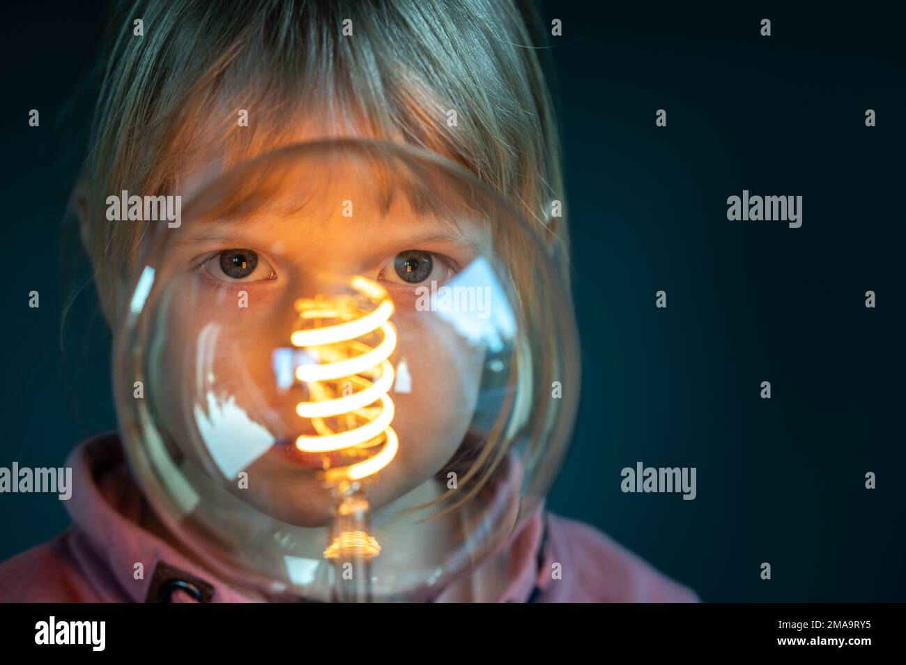 Young child looks concentrated through a filament light bulb. Symbol for a child curiously discovering the world. Stock Photo