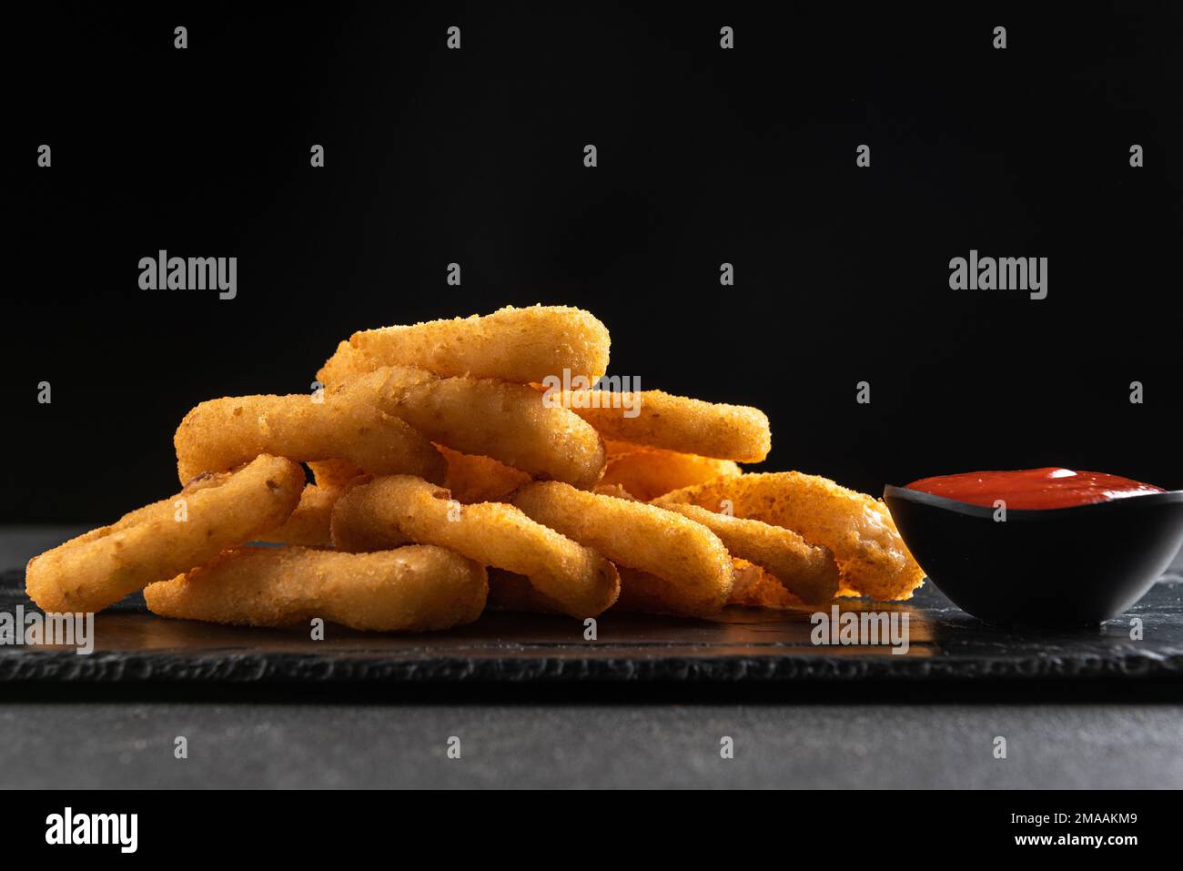 Calamari rings deep-fried in breading. Crispy squid rings on a dark