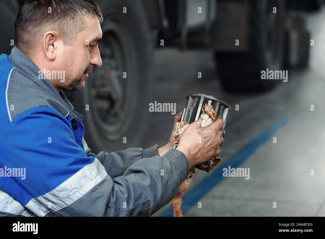 Auto mechanic repairs truck. Professional repair and diagnostics of cargo tractors and equipment. Mechanic in workshop considers spare parts.. Stock Photo