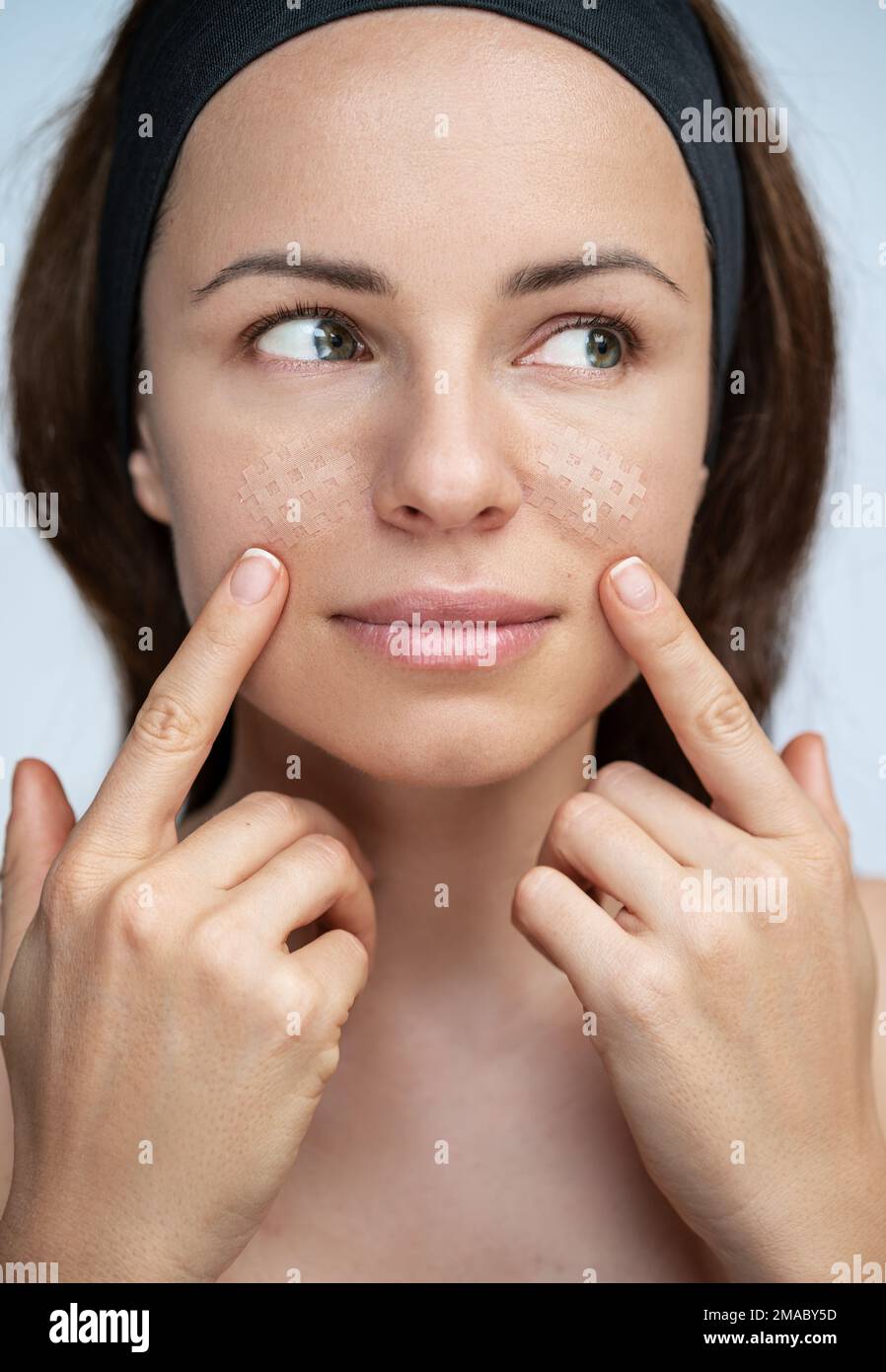 Young adult woman applying facial kinesio tapes on her face, facial