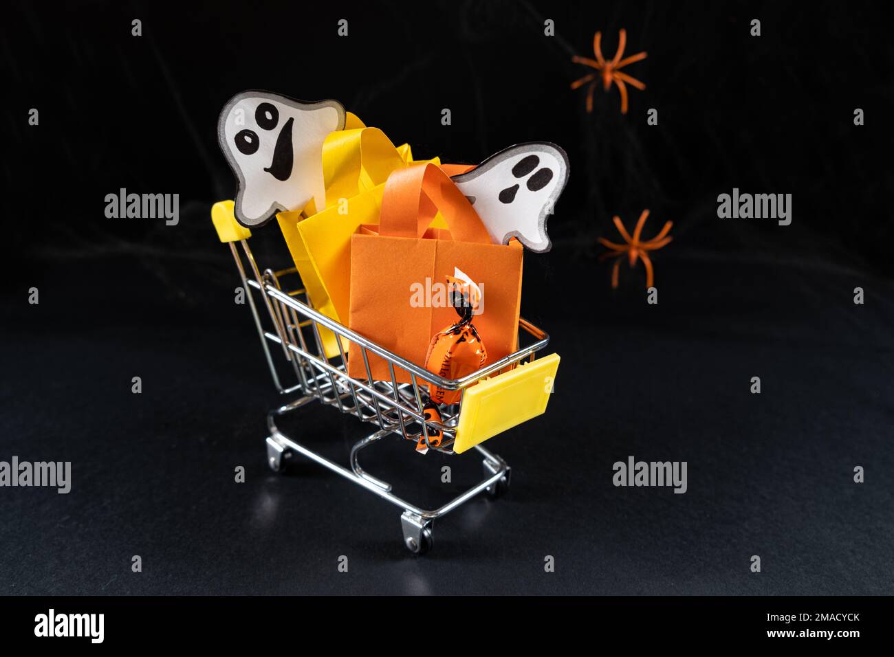 A small cart with bags, gifts and ghosts on the black background. Halloween Sale, copy space for text. Stock Photo