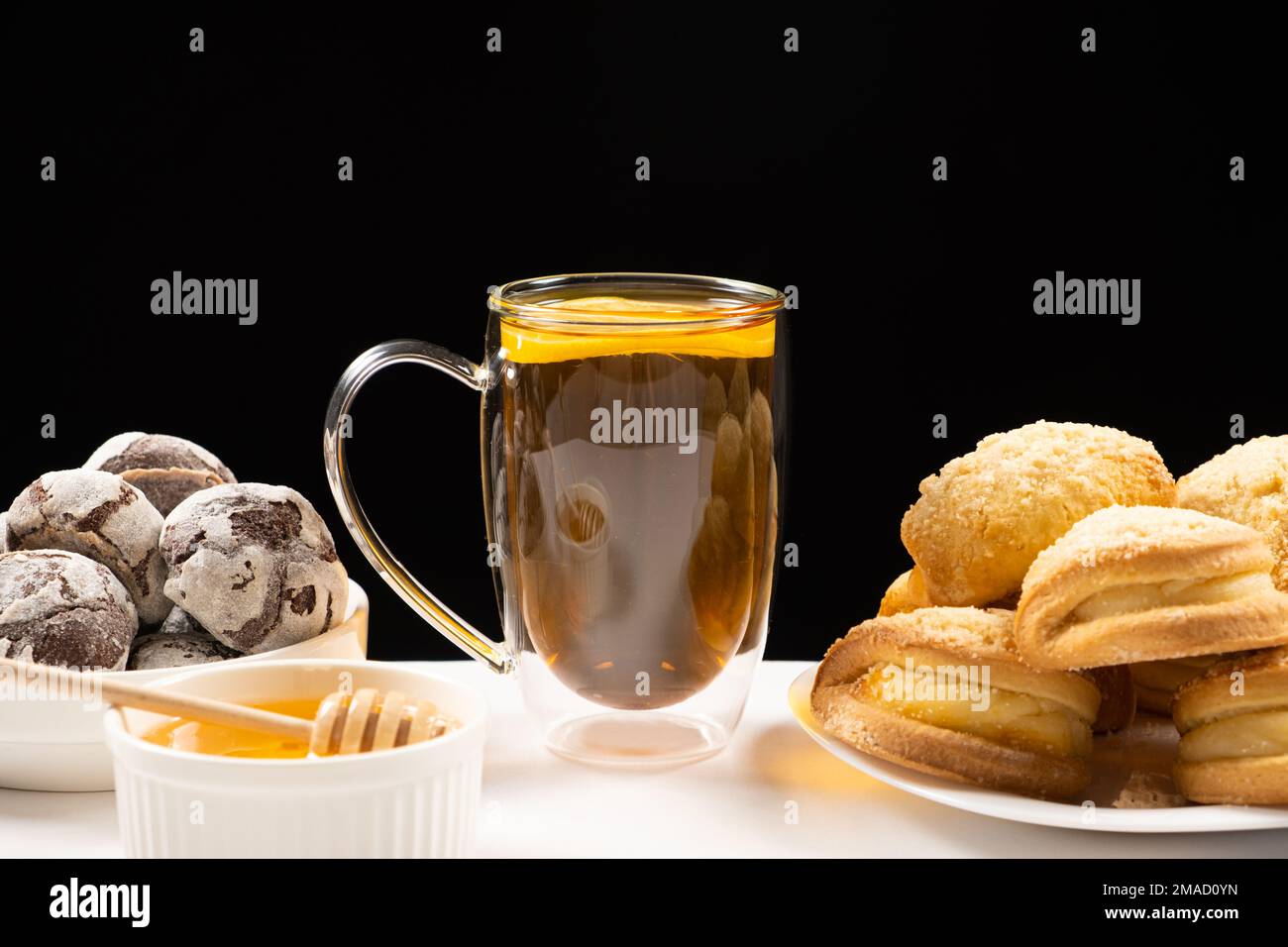 Tea with lemon and honey with cocoa cookies and cakes with creamy filling on a black background. Stock Photo