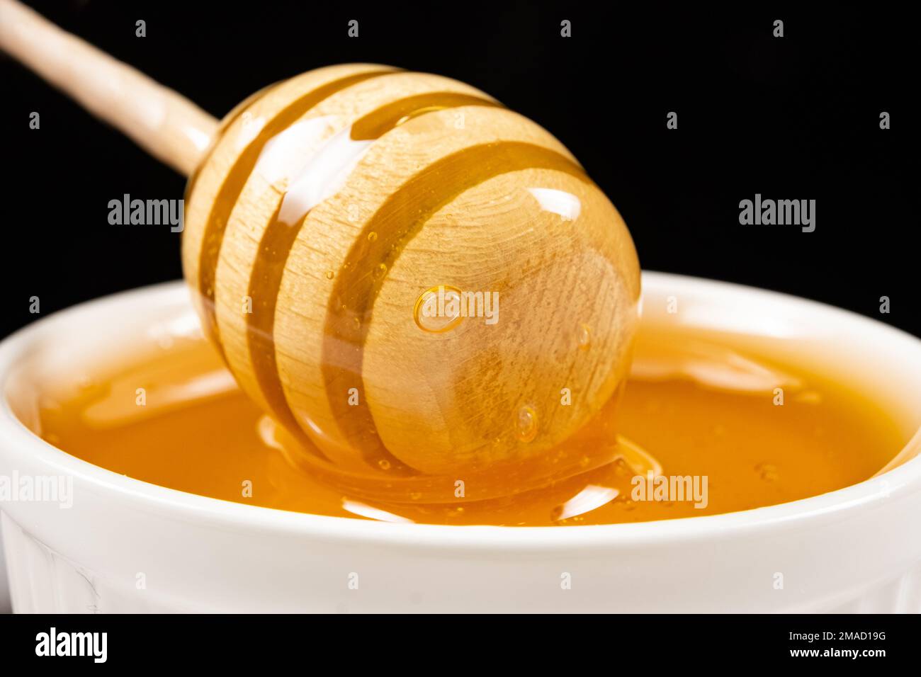 Liquid natural bee honey in a white ceramic bowl with a wooden spoon. Stock Photo