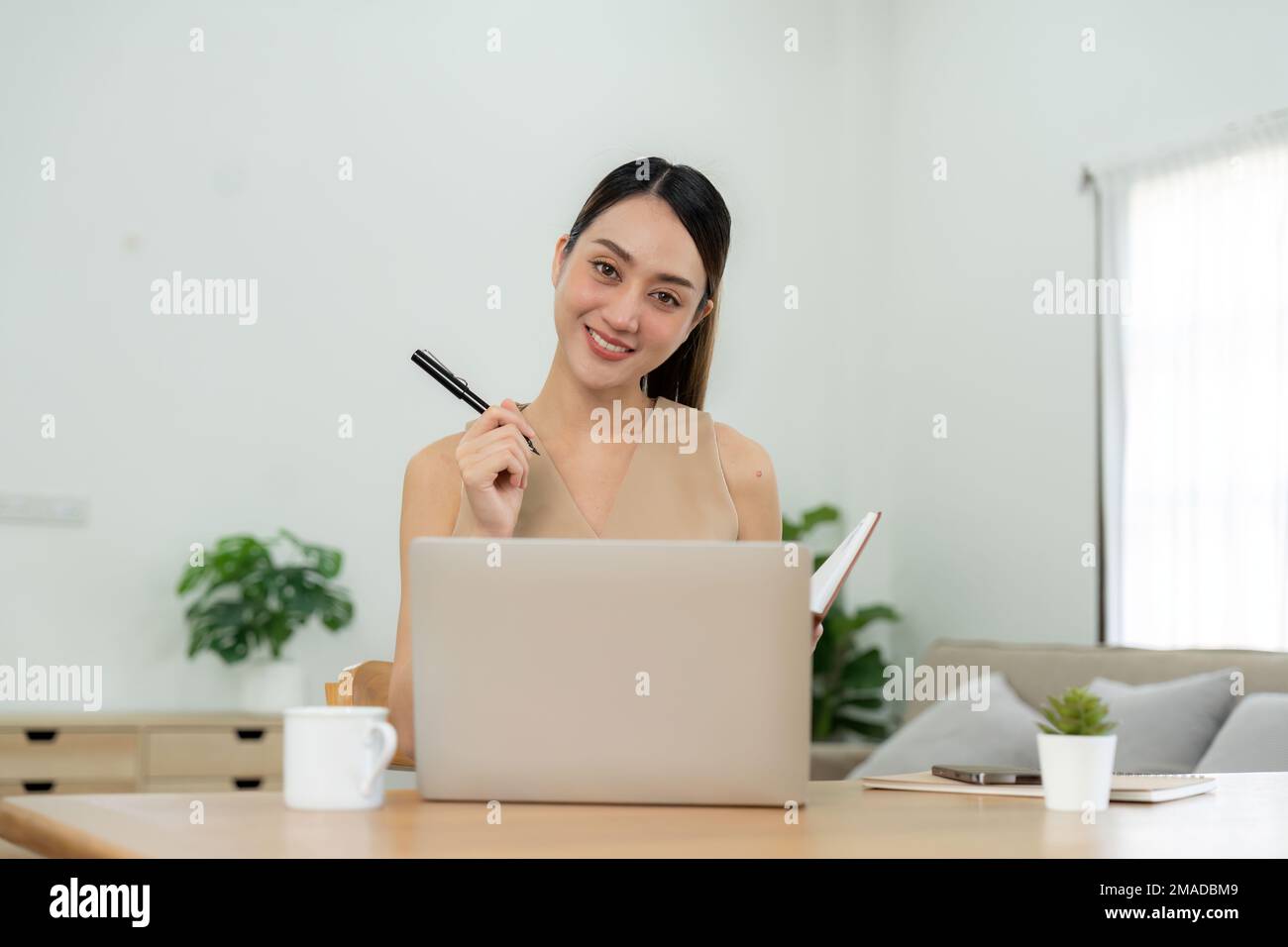 Young asian woman taking down notes in diary. Female university student preparing note for the exam at home office, online education and work from Stock Photo