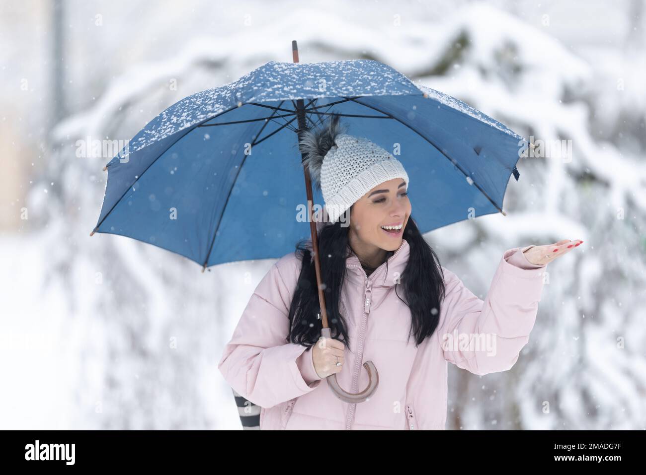 Happy woman holding umbrella on the cold snowy day snowflakes fall on her hand. Stock Photo