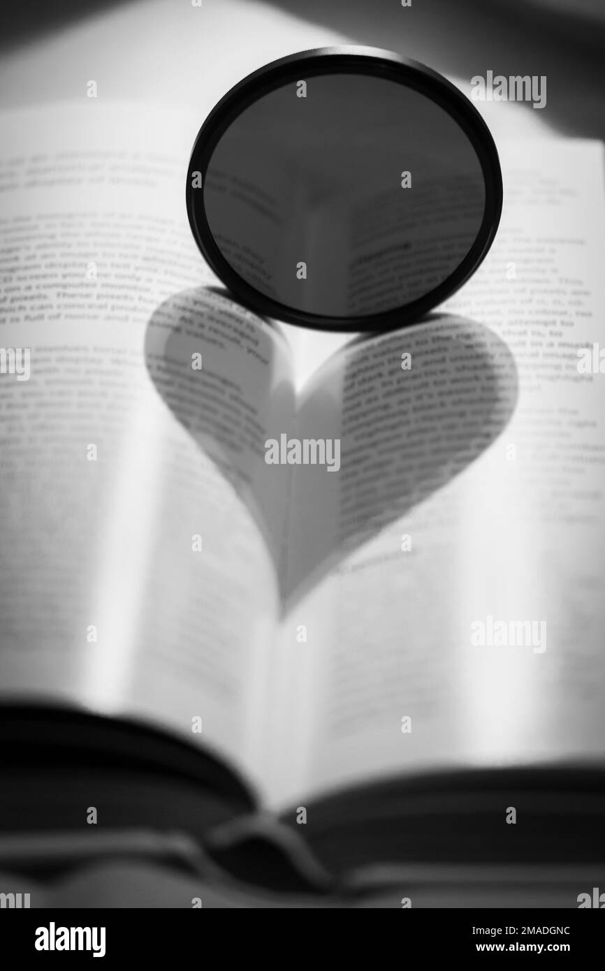 Heart Shape Shadow Over Open Book With Camera Lens Filter Stock Photo