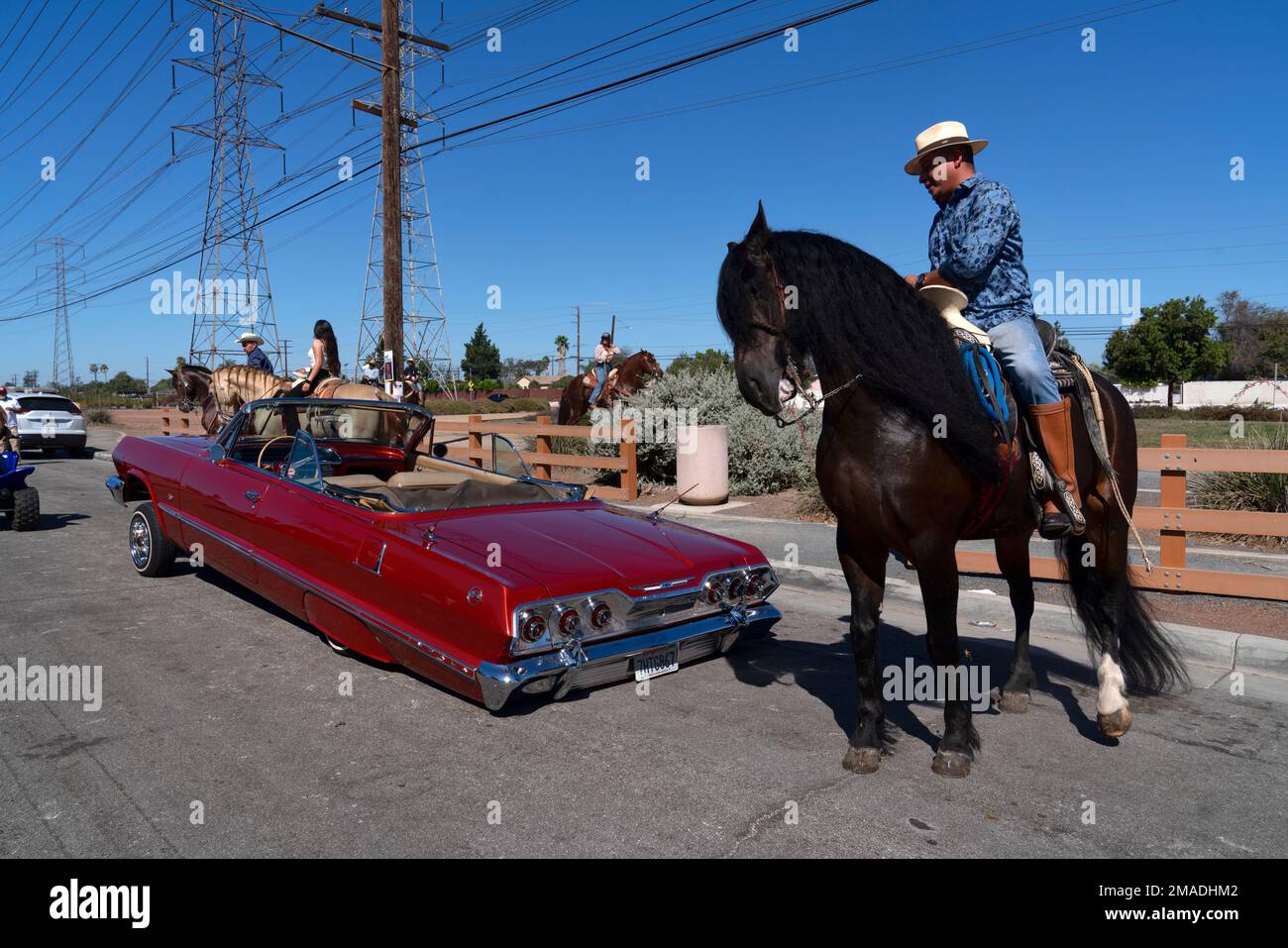 A riders maneuvers his horse around a classic car on the street prior