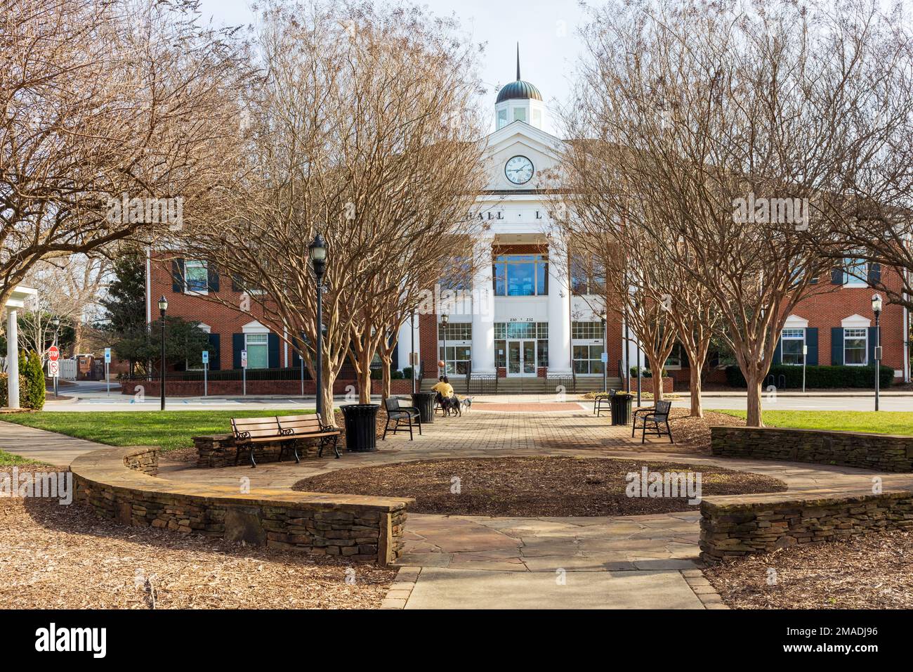 MATTHEWS, NC, USA-15 JANUARY 2023: Matthews Town Hall and Library, and park, with two people sitting on bench with two dogs.  Sunny day. Stock Photo