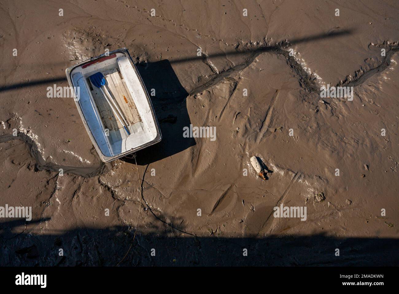 Dingy in the Mud: A small rectangular dingy with two oars is stranded in the chocolate brown tidal mud of Penryn Harbour. Shot from above. Stock Photo