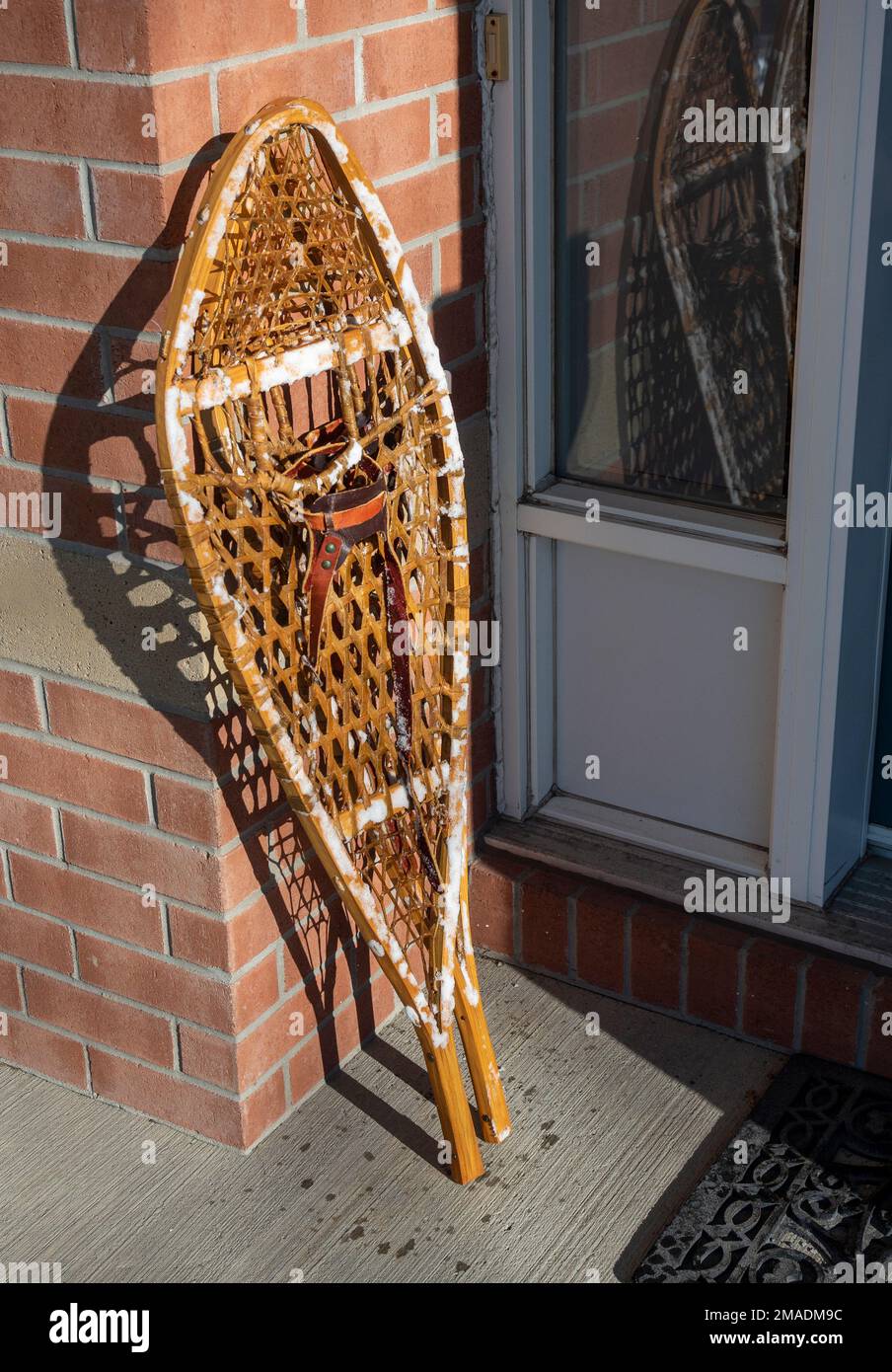 Snowshoes stacked by the front door: A pair of traditional snowshoes stacked in a sunny spot by the front door of a house.  The shoes are still covered with snow. Stock Photo