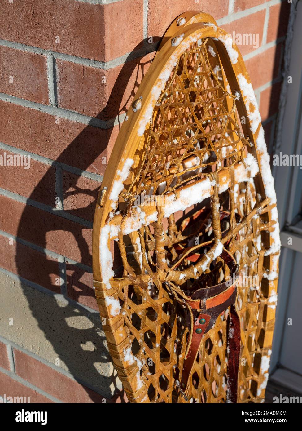 Snowshoes stacked by the front door closeup: A pair of traditional snowshoes stacked in a sunny spot by the front door of a house.  The shoes are still covered with snow. Stock Photo