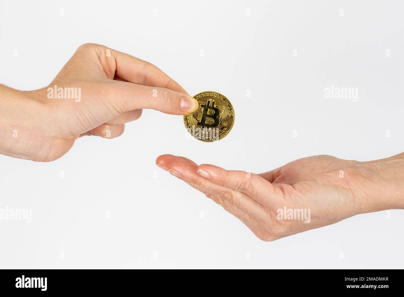 woman's hand giving a bitcoin coin to another woman on white background Stock Photo