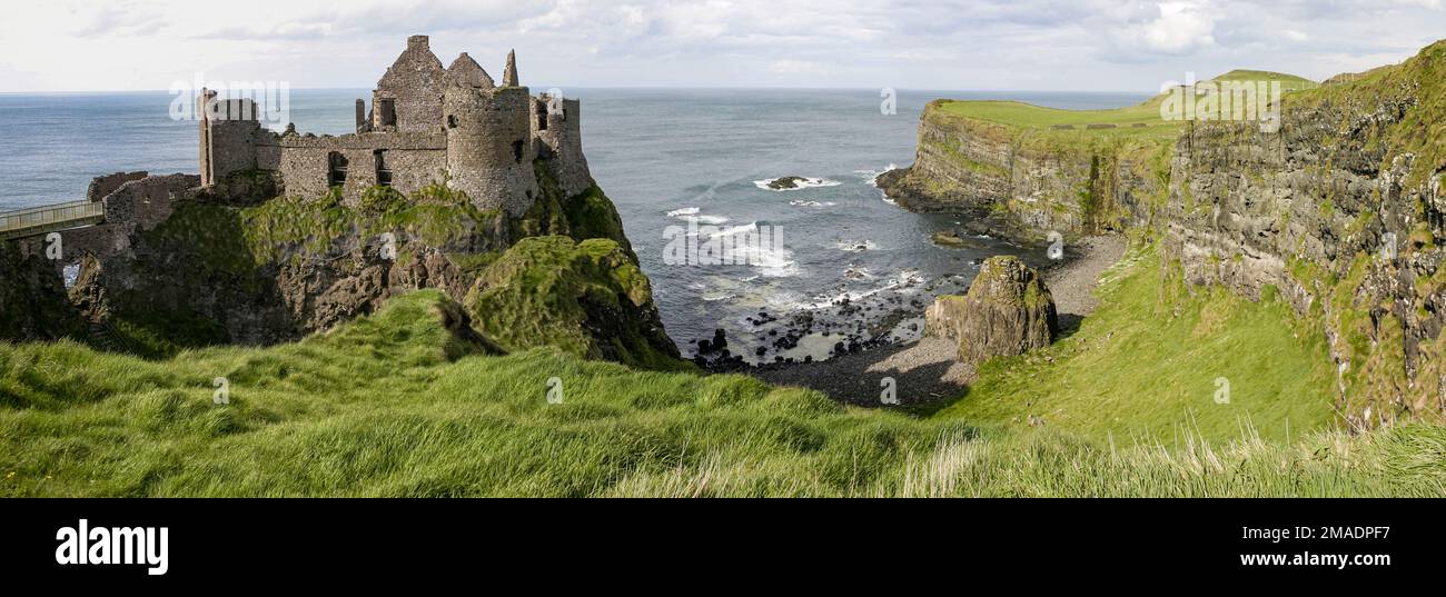 Dunluce Castle Ruin: A cliff edged headland, a small bay and a medow covered in long green grass leads out to the ruin on the edge. Stock Photo