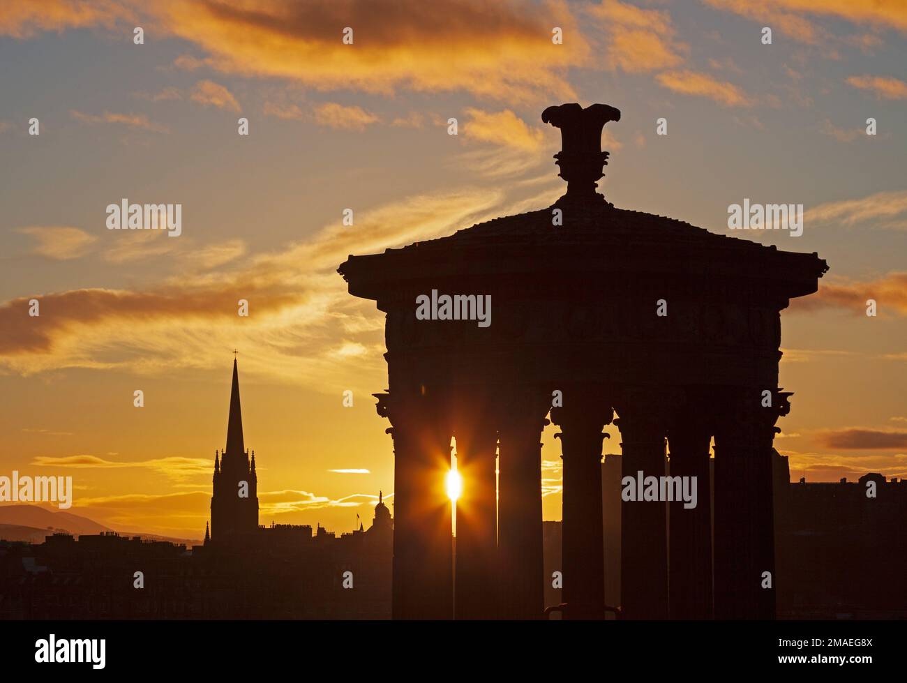 Calton Hill and Edinburgh city centre, Scotland, UK. 19th January 2023. Twinkling cool sunset at 4 degrees centigrade, pictured through the historic architecture of the Dugald Stewart monument and the spire of The Hub in the background. Credit: Archwhite/alamy live news. Stock Photo