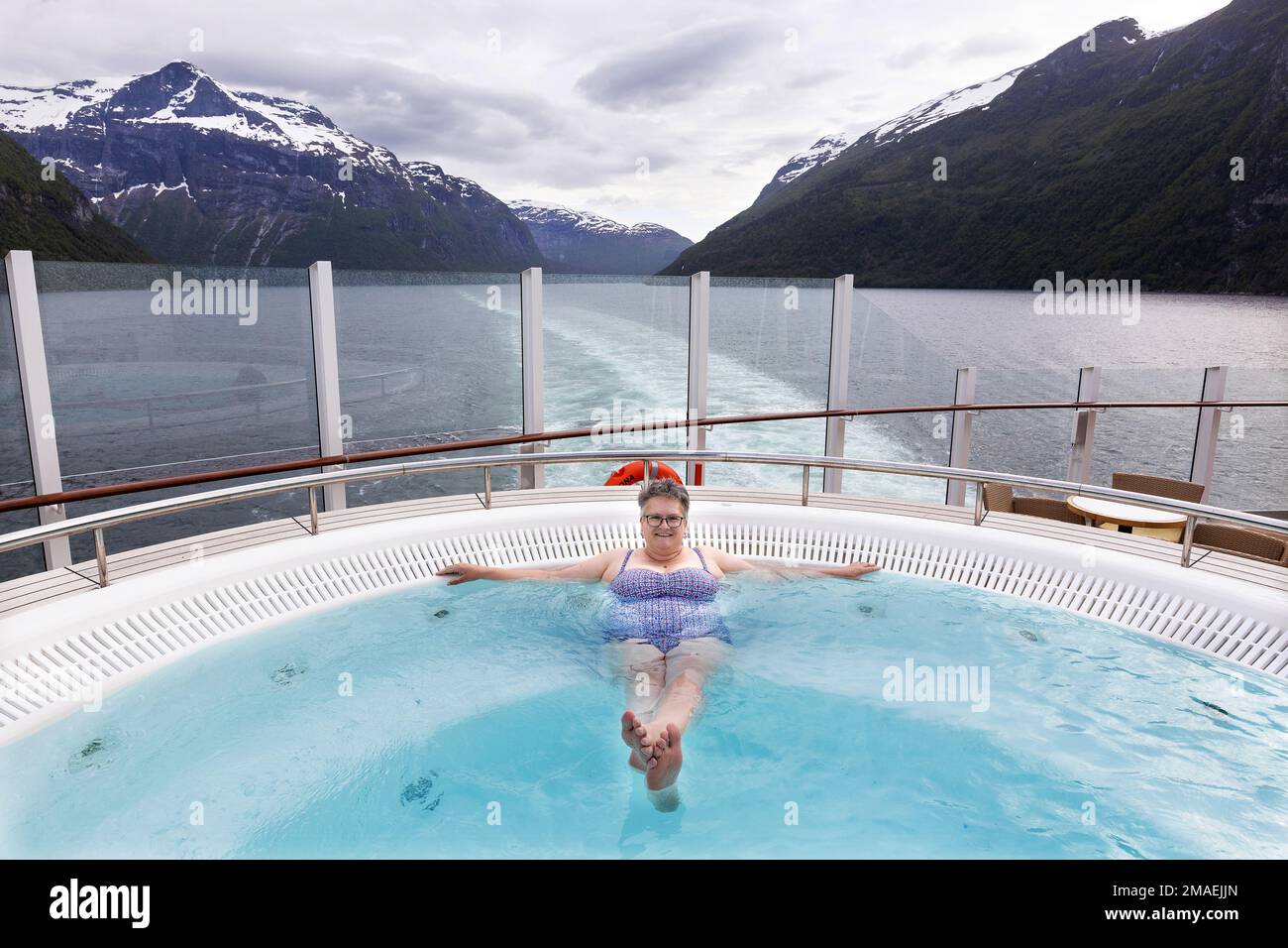 A tourist enjoys the spectacular views while resting in the hot top aboard a cruise ship n a Norweigan fjord. Stock Photo