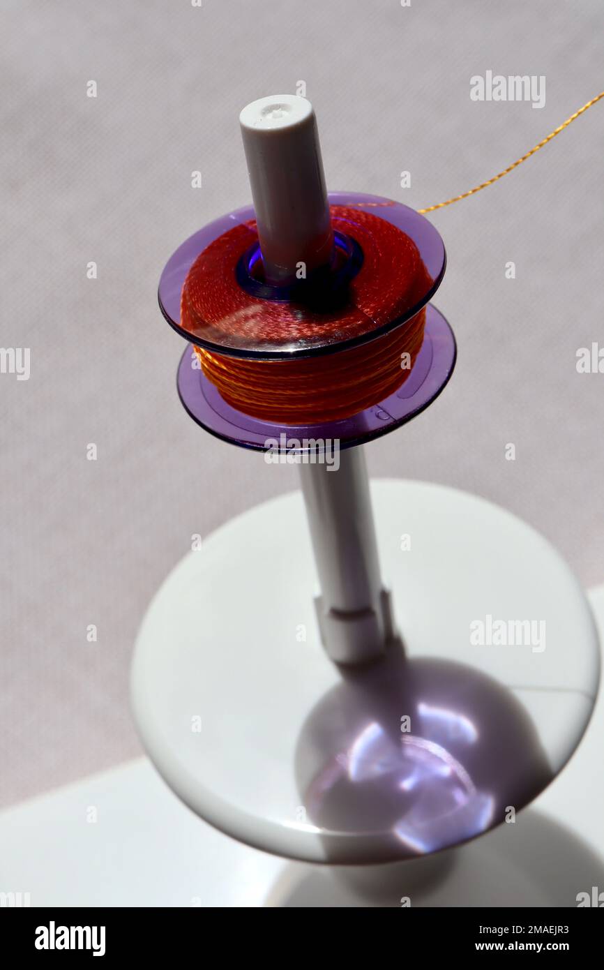 Macro of intense yellow rayon yarn on a semi-transparent purple plastic cylinder called Bobbin (used in sewing machines), with sunlight creating colou Stock Photo