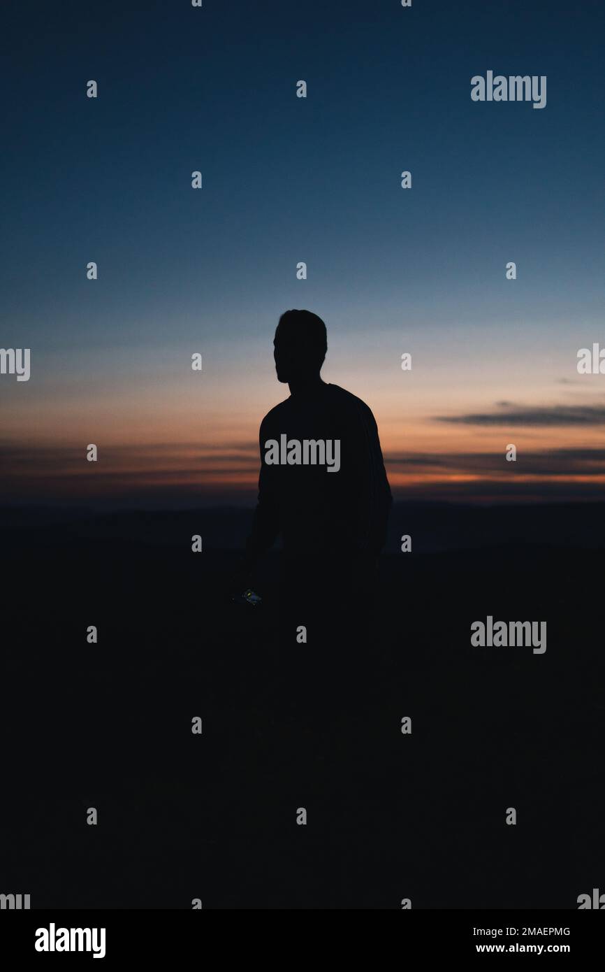 Silhouette of a man during sunset with orange and blue sky Stock Photo ...