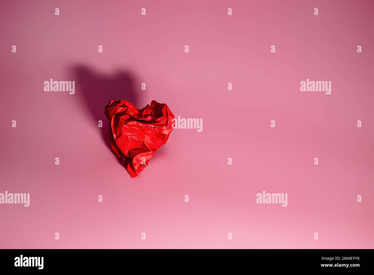 Red heart of rumpled paper on a Pink background with shadow. Valentine's Day Concept. A symbol of separation, sadness Stock Photo