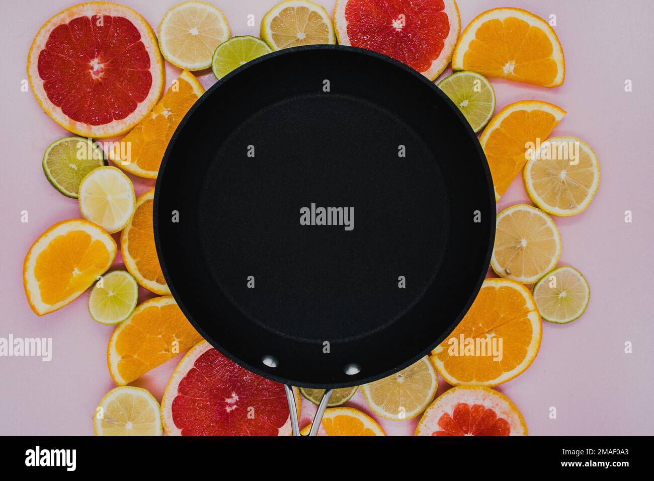 Black frying pan on sliced citrus plants. Oranges, grapefruit, lemon, lime on a pink background. flat lay Stock Photo