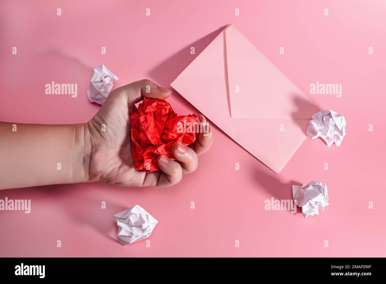 hand of aggressive and frustrated man squeezing heart out of crumpled paper. envelope with lumps of paper scattered. Letter to a Loved One on Valentin Stock Photo