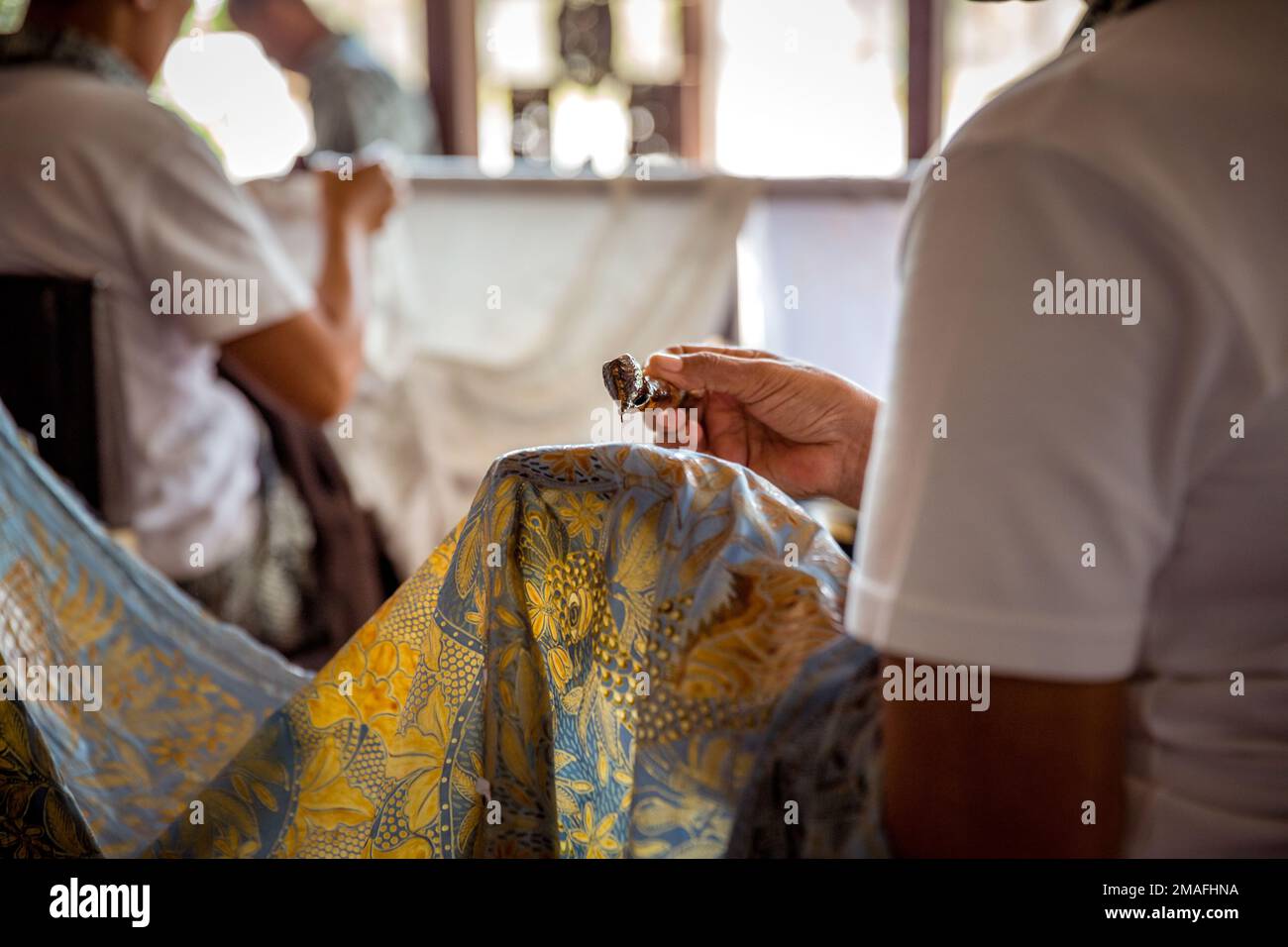 Indonesian male and female artists drawing batik on blue fabric in a touristic atelier. Close up shot from the back. Stock Photo