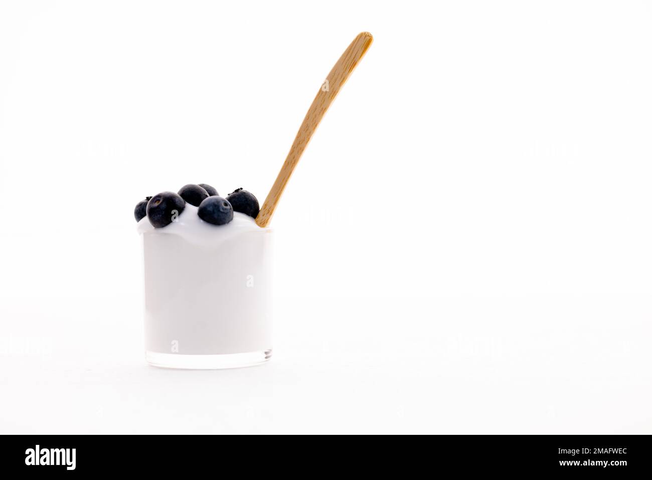 Isolated bio plain Greek yoghurt with blueberries and a wooden spoon against a deep white background Stock Photo
