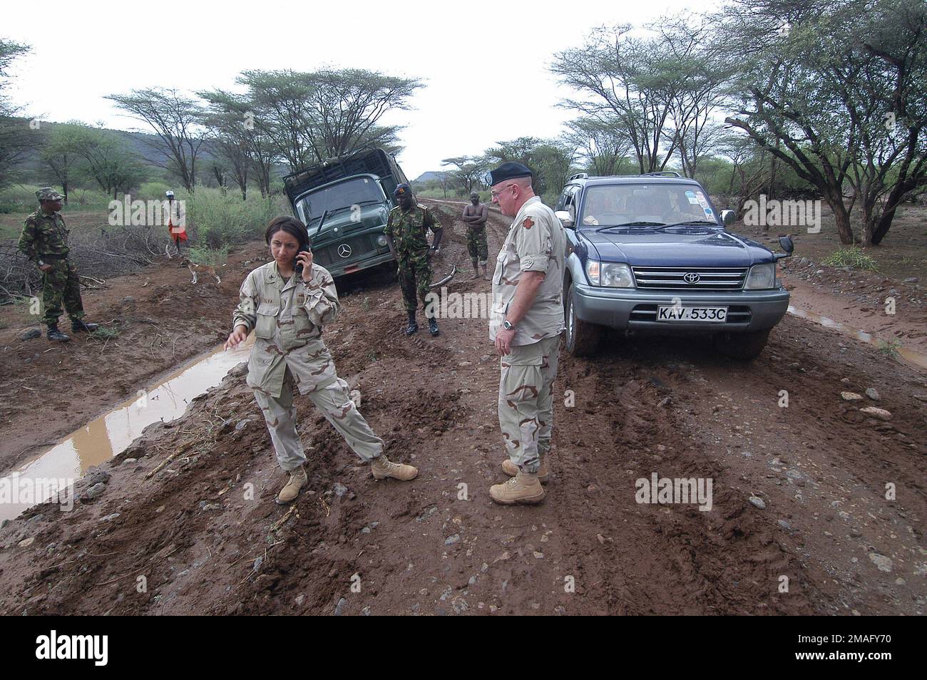 060804-N-0411D-003. [Complete] Scene Caption: U.S. Navy Operations SPECIALIST 2nd Class (SW/AW) Jessica Silva, left, uses an Iridium phone to call for assistance to help members of the Kenyan Army forces free a vehicle which got stuck in the mud during Exercise Natural Fire at Nginyang, Kenya, on Aug. 4, 2006. Rain made portions of a one-lane road along the Nginyang River difficult to traverse. The 10-day multi-lateral field training exercise involves military personnel from East African Community nations, U.S.-based units and Combined Joint Task Force-Horn of Africa. The exercise will focus o Stock Photo