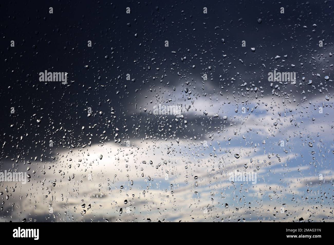 Raindrops on window glass on blurred background of sky with storm clouds. Beautiful water drops, weather during rain Stock Photo