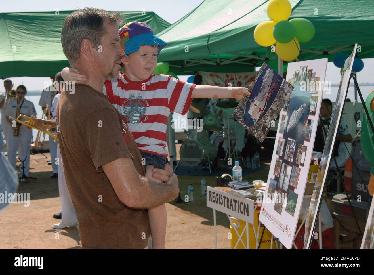 060903-N-6501M-002. [Complete] Scene Caption: An Australian father and son look at a display board showing photographs of the U.S. Navy Military Sealift Command Mercy Class Hospital Ship USNS MERCY (T-AH 19) at sea while attending a NAPCAN Foundation sponsored'Fishing Fun Day,'being held in the city of Darwin, Northern Territory, Australia, on Sept. 3, 2006. The NAPCAN Foundation is dedicated to the prevention of child abuse and they use these family events to get their message across. In the background the U.S. Navy Show Band, embarked with the Medical Treatment Facility aboard the MERCY, is Stock Photo