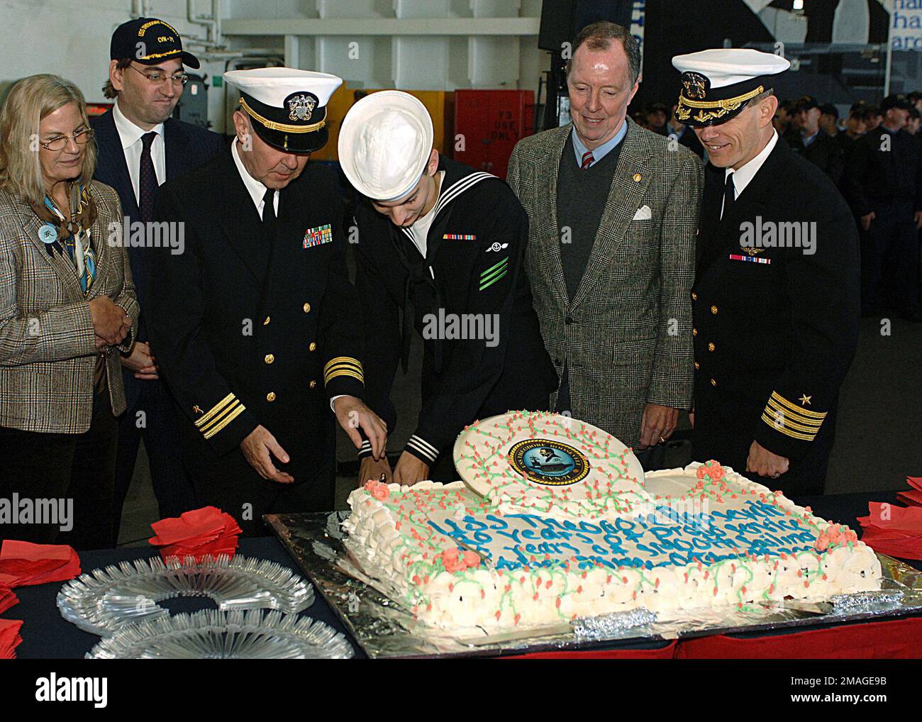 061025-N-6266K-002. [Complete] Scene Caption: U.S. Navy CAPT. John R. Haley (right), Commanding Officer, Nimitz Class Aircraft Carrier USS THEODORE ROOSEVELT (CVN 71); and U.S. Navy (retired) Rear Adm. Paul W. Parcells (second from right), first Commanding Officer, USS THEODORE ROOSEVELT, watch as LT. CMDR. Donald Moss (third from left), Chaplain and oldest ROOSEVELT crew member, and AIRMAN Andrew Bryan (third from right), the youngest ROOSEVELT crew member, prepare to cut the anniversary cake during the ceremony honoring the 20th Anniversary of the commissioning of the ROOSEVELT, while it is Stock Photo