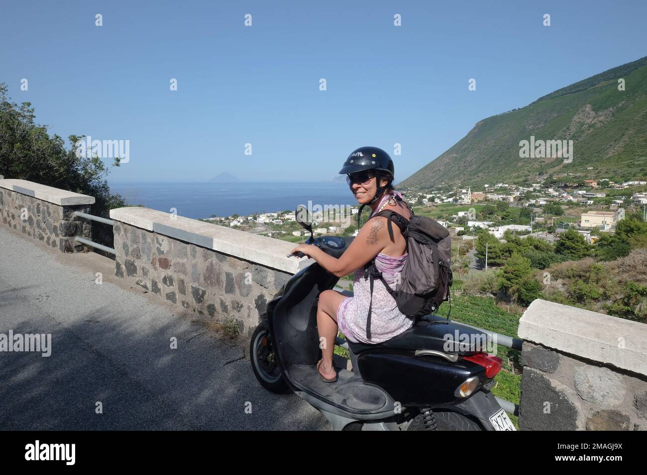 Girl wearing a helmet riding a bike on the Aeolian Island of Salina, Sicily, Italy Stock Photo