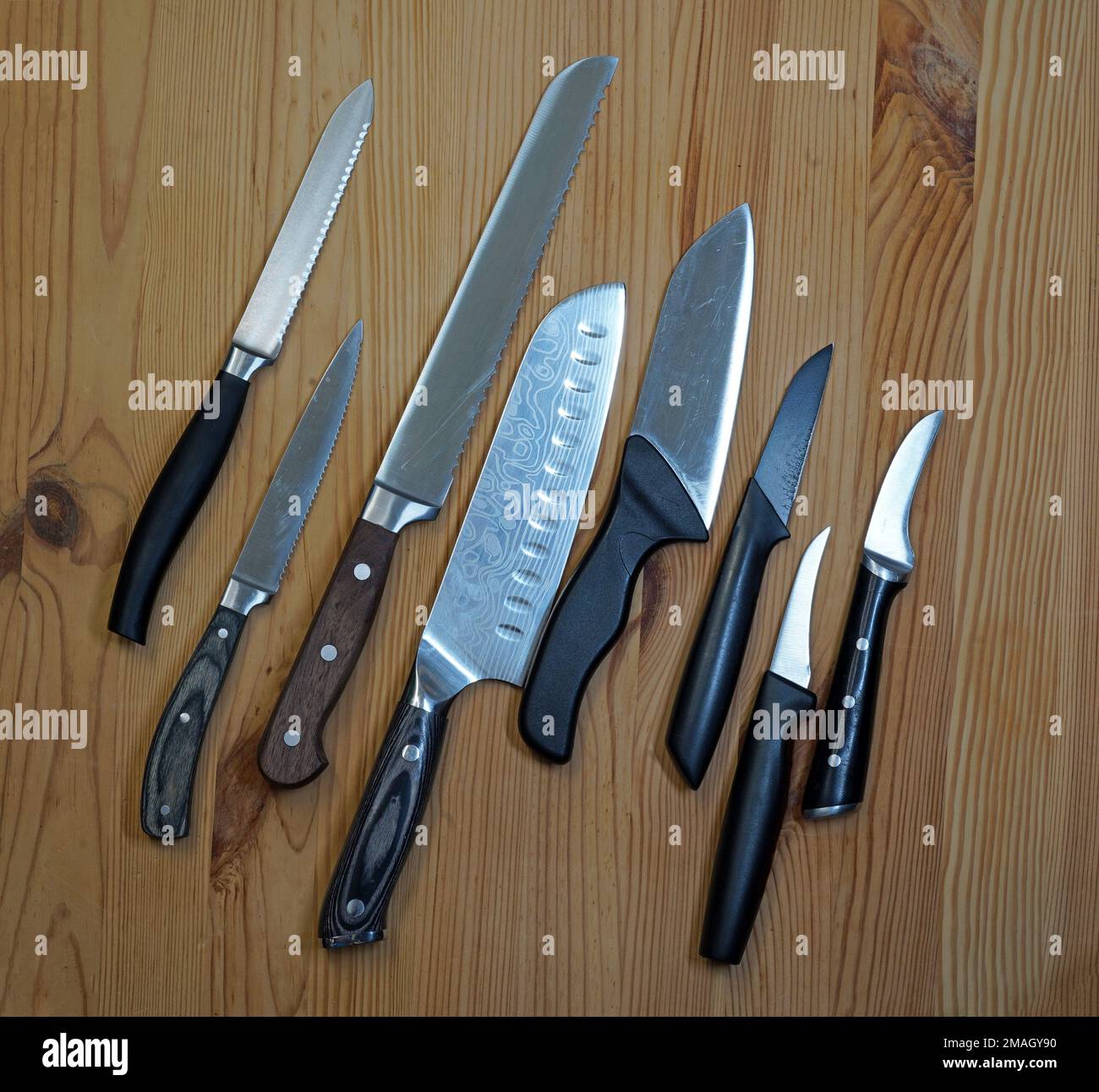 Eight kitchen knives on wooden board. The first is a tomato knife, the third a bread knife. Next a Japanese Gyuto knife. Stock Photo