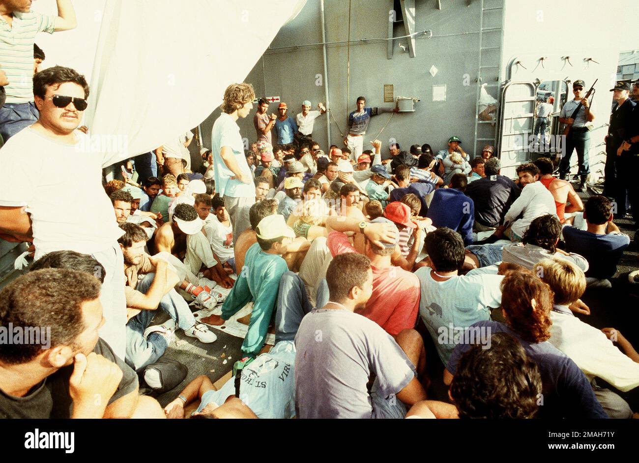 PETTY Officer (EWSN) Tom Tucker (far right with shotgun) stands guard duty over Cubans, who are fleeing Cuba, aboard USS GALLERY (FFG-26). Subject Operation/Series: SEA SIGNAL V Base: Naval Station, Guantanamo Bay Country: Cuba (CUB) Stock Photo